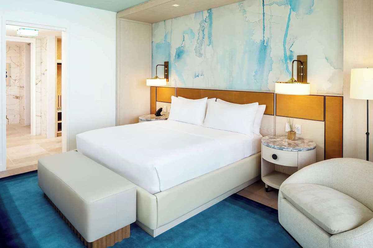 Une chambre d’hôtel moderne avec un grand lit, des tables de chevet, une chaise et une moquette bleue.