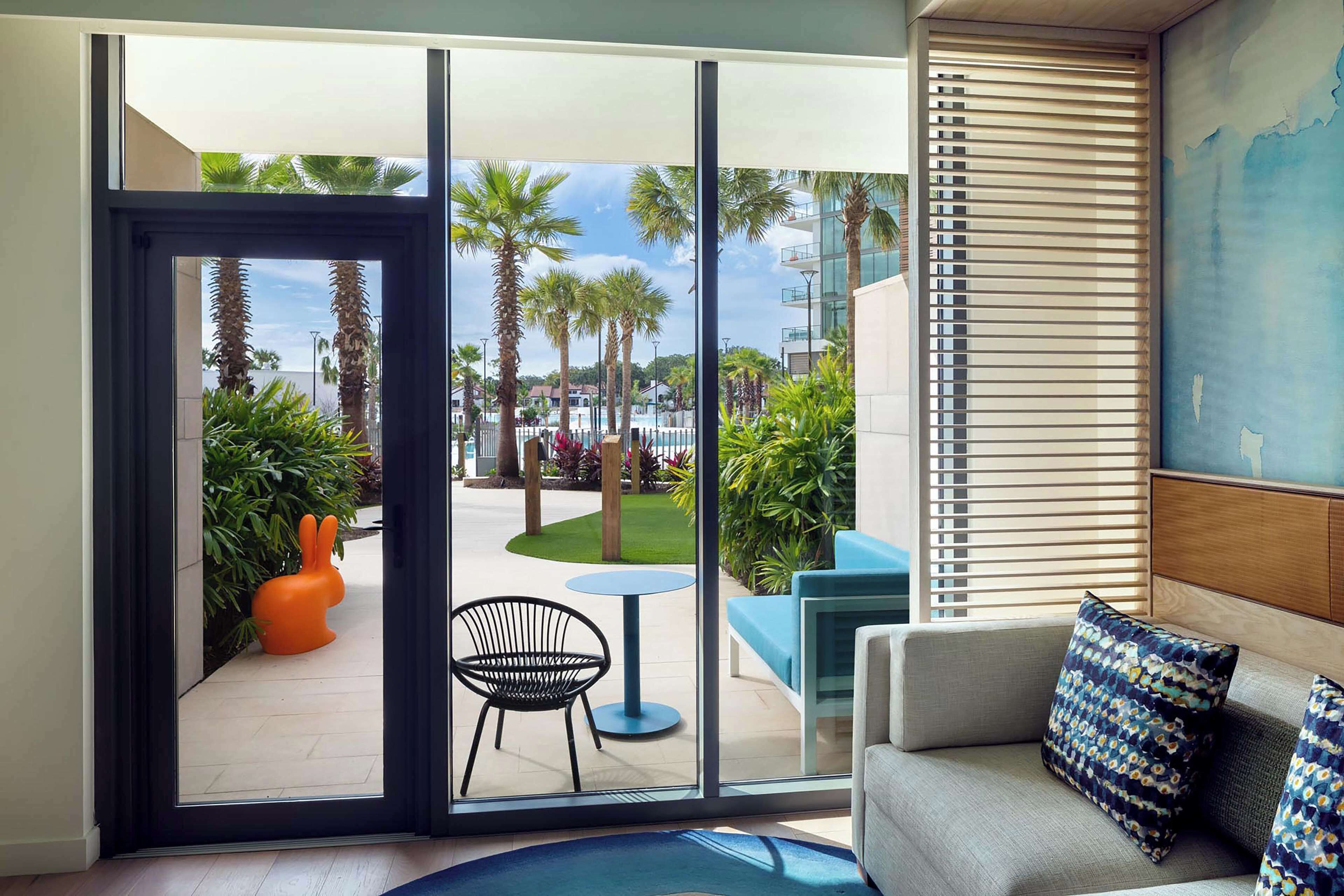 Una habitación moderna con un amplio ventanal corredera que da a un patio exterior con palmeras y una silla azul.
