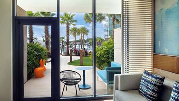 Una habitación moderna con un amplio ventanal corredera que da a un patio exterior con palmeras y una silla azul.