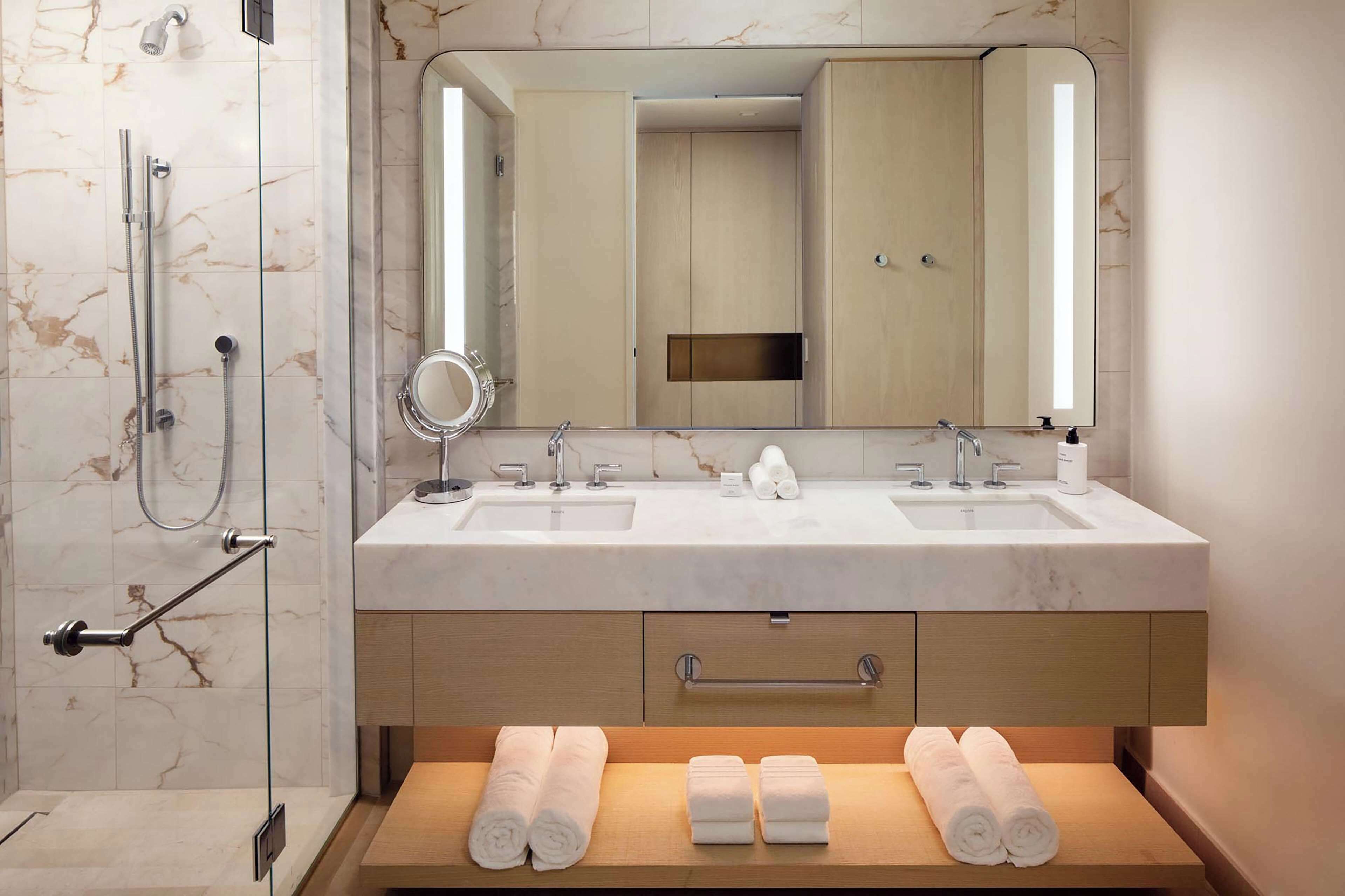 A modern bathroom with two sinks, a shower, a mirror, and a wooden vanity with towels.