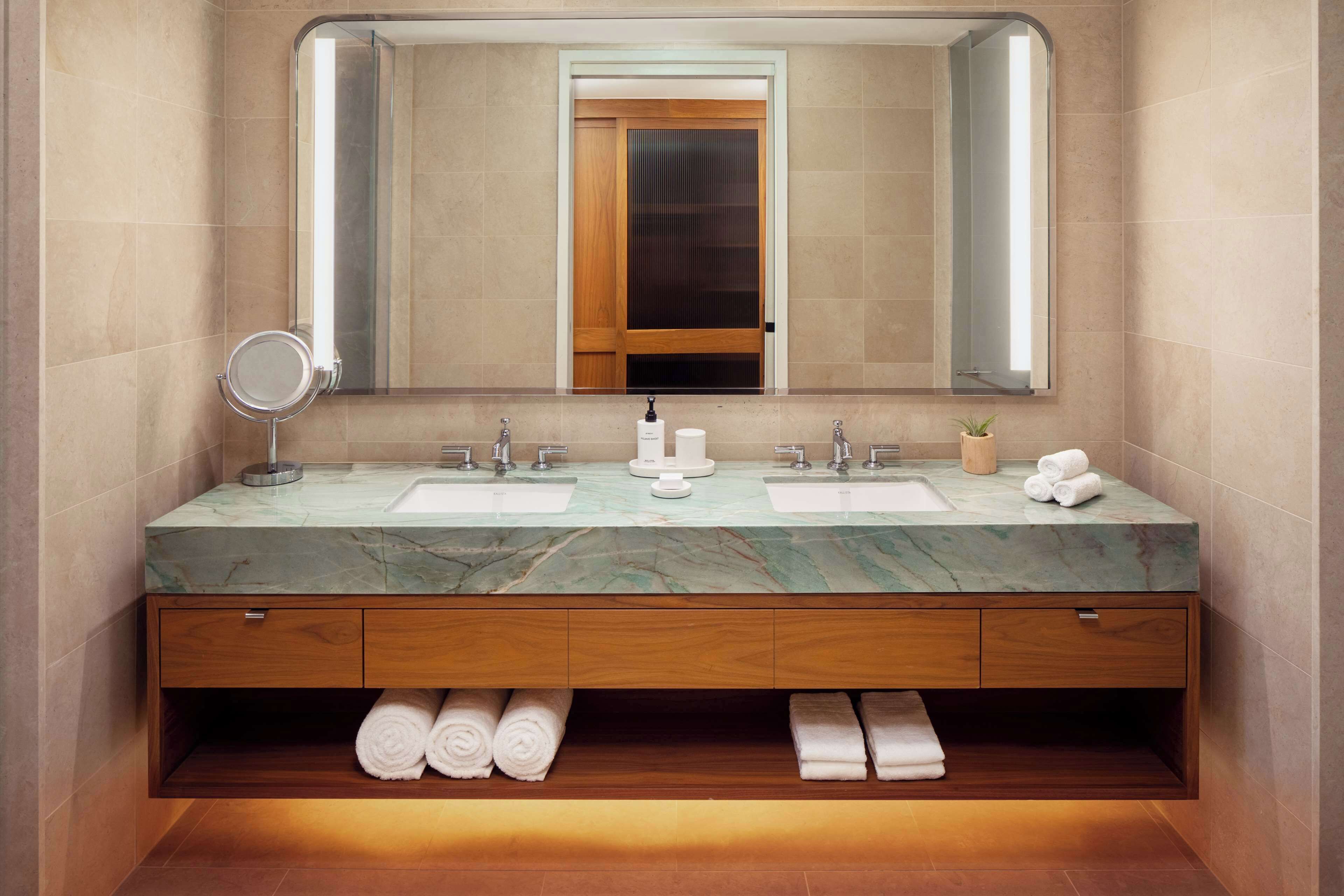 Un baño moderno con dos lavamanos, un espejo grande y un mueble de tocador de madera con espacio para toallas.