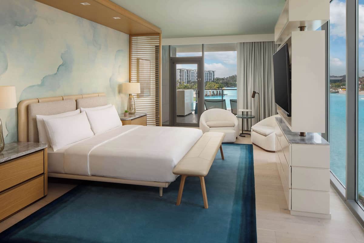 Une chambre d’hôtel moderne dotée d’un grand lit, d’un bureau, d’une chaise, d’une télévision et offrant une vue sur l’océan.
