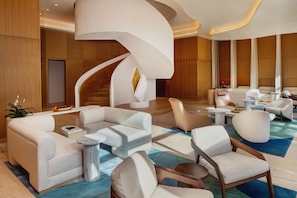 A modern lobby with a curved staircase, plush seating, and a wooden finish.
