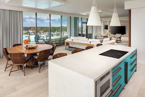A modern living room with a large island, dining area, and a view of the outdoors.