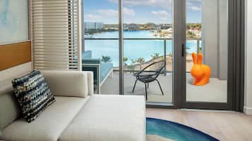 Un salon moderne avec un canapé, un coussin à motifs et une vue sur une piscine et des immeubles, visible à travers une porte vitrée.