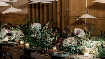 Een eettafel gedekt met borden, bestek en kaarsen, omringd door bloemdecoraties en hanglampen.