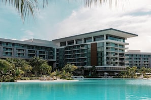 A modern hotel with multiple balconies, a pool, and palm trees.