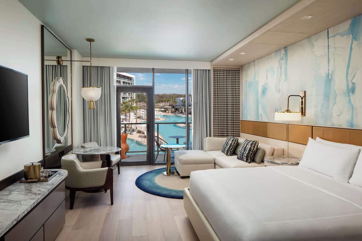 Une chambre d’hôtel équipée d’un lit, d’un bureau, d’une chaise, d’une petite table et offrant une vue sur une piscine.