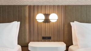 A hotel room with a wooden panel wall, a built-in vanity with a mirror, and two beds with white bedding.