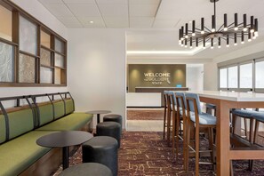 A modern hotel lobby with a reception desk, a green sofa, round tables, and a bar area. - Hampton Inn Stockton, Ca (Stockton)