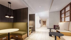 A modern hotel lobby with a seating area, a long corridor, and a reception desk.