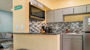 A kitchen with a central island, bar stools, a microwave, a refrigerator, and a backsplash with a geometric pattern.