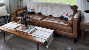Een gezellige woonkamer met een leren bank, een houten salontafel en uitzicht op een groen landschap door een groot raam.
