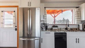 A modern kitchen with white cabinets, stainless steel appliances, and a window with a view of trees. - Frontier Farmhouse,Cal-K,Sauna, HT, MountainViews (Port Angeles)