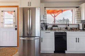 A modern kitchen with white cabinets, stainless steel appliances, and a window with a view of trees. - Frontier Farmhouse,Cal-K,Sauna, HT, MountainViews (Port Angeles)