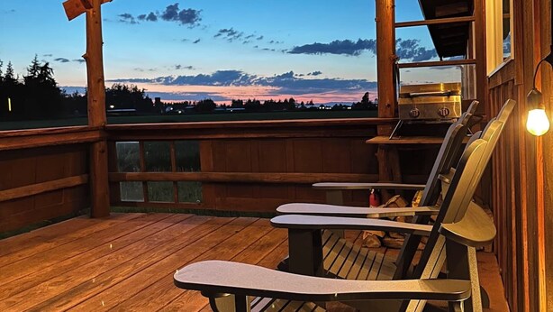 Een houten terras met uitzicht op de bergen, een barbecue en twee Adirondack-stoelen.