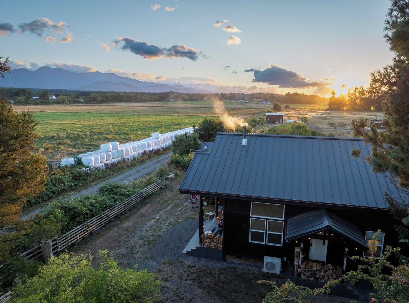 A rural property with a barn, hay bales, and a view of mountains.