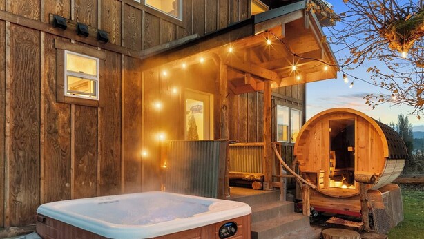En stuga byggd av trä med ett bubbelbad, en bastu i form av en trätunna och ljusslingor.