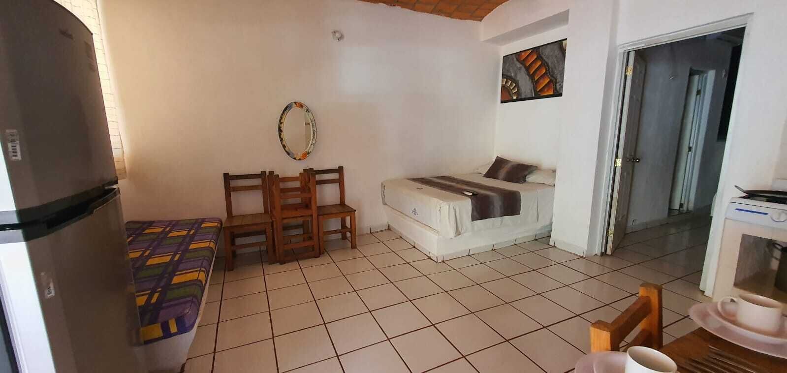 A compact room with a bed, a small table, and a chair. There is a refrigerator on the left and a microwave on the right.