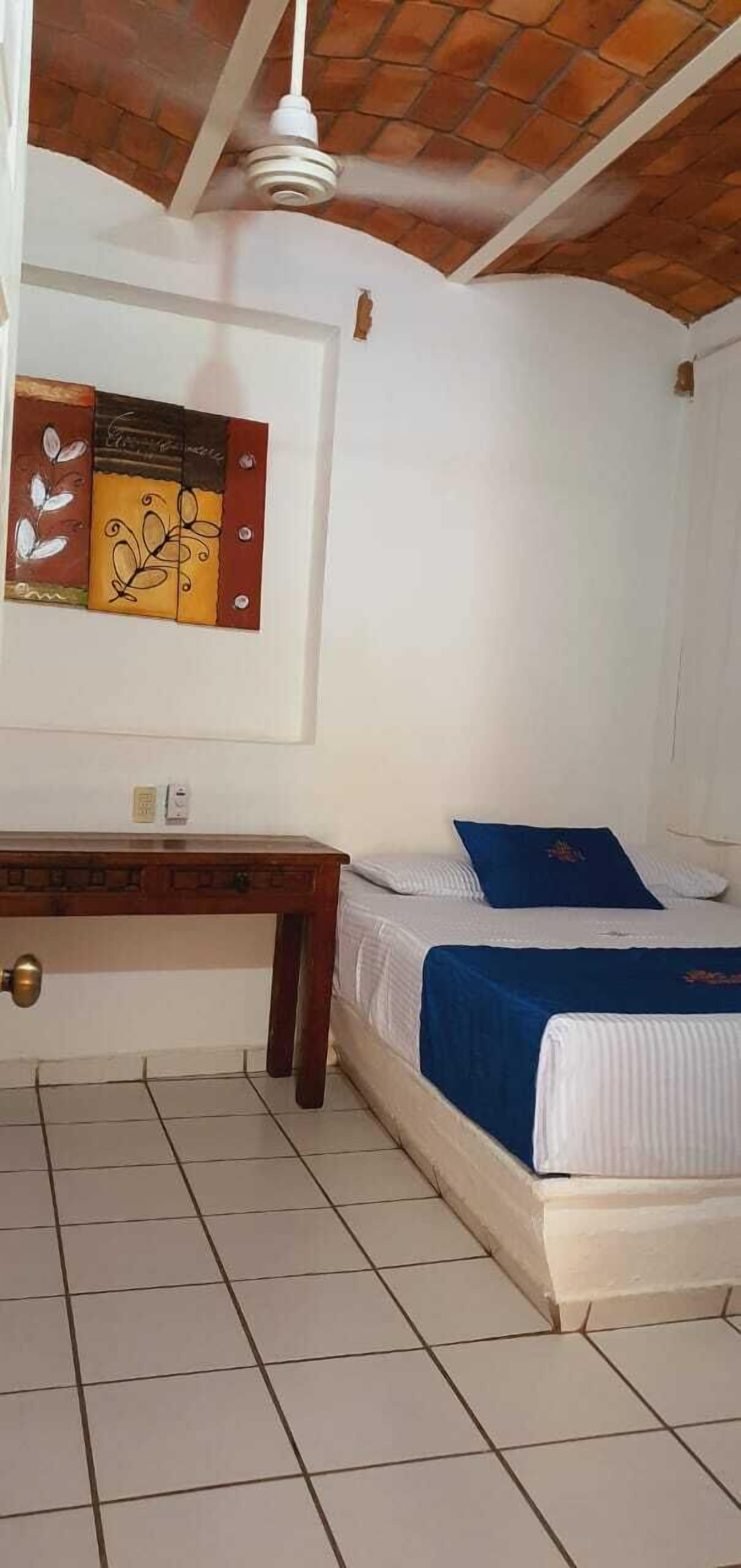 A bedroom with a bed, a nightstand, a wall-mounted artwork, and a ceiling fan.