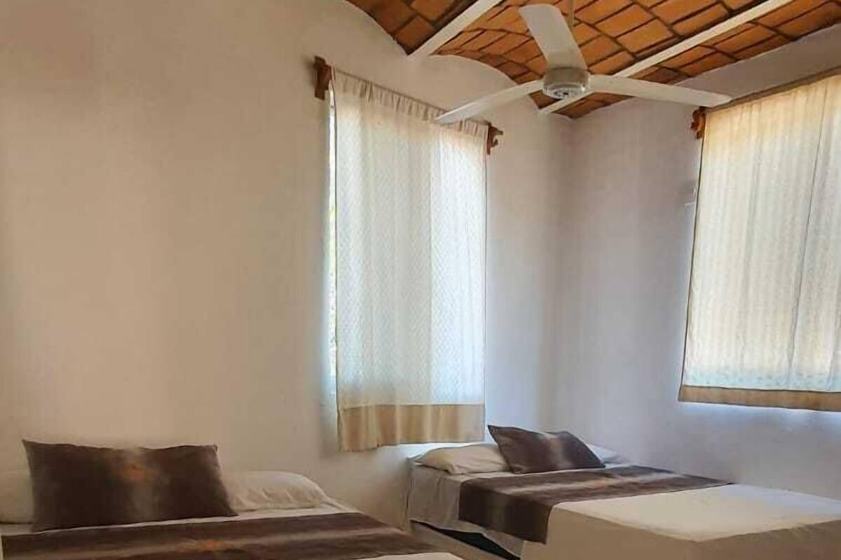 A room with two beds, a ceiling fan, and windows with curtains.