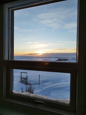 A room with a large window overlooking a snowy landscape and a sunset. - Guesthouse Hateigi (Rangárþing ytra)