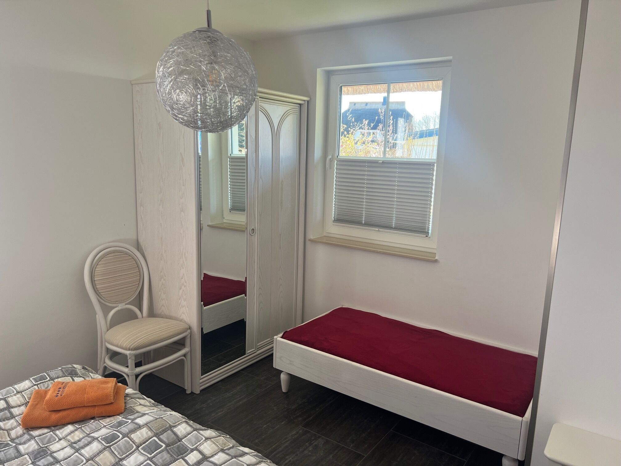 A bedroom with a single bed, a chair, a mirror, and a window with blinds.