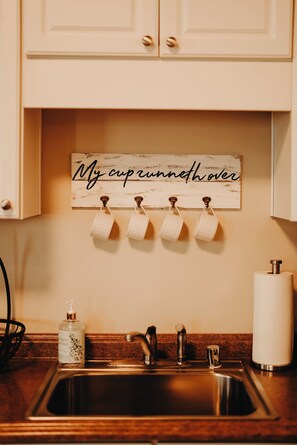 Una cocina con un lavamanos de acero inoxidable, un dispensador de jabón y un toallero de papel con un cartel arriba.