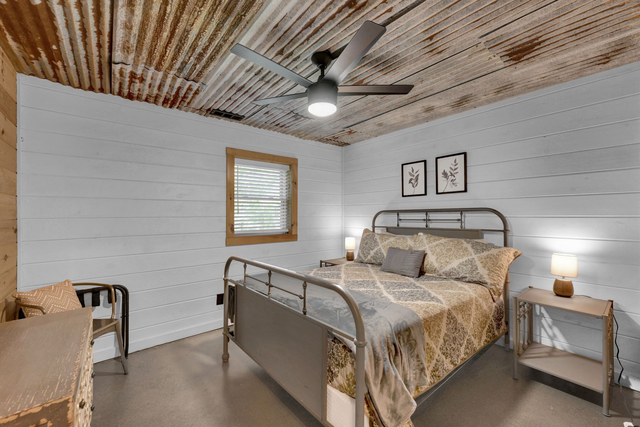 Une chambre à coucher avec un cadre de lit en métal, une tête de lit en bois, une table de chevet avec une lampe et une fenêtre avec des stores.