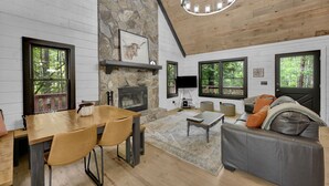A cozy cabin interior with a stone fireplace, wooden dining table, and a comfortable seating area.