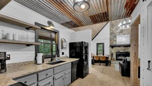 A modern kitchen with granite countertops, a black refrigerator, and a dining area with a stone fireplace.