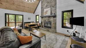 A spacious living room with a stone fireplace, wooden ceiling, and a large TV.