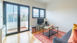 Una sala de estar moderna con balcón, un televisor de pantalla plana, una mesita con un control remoto y una maleta.