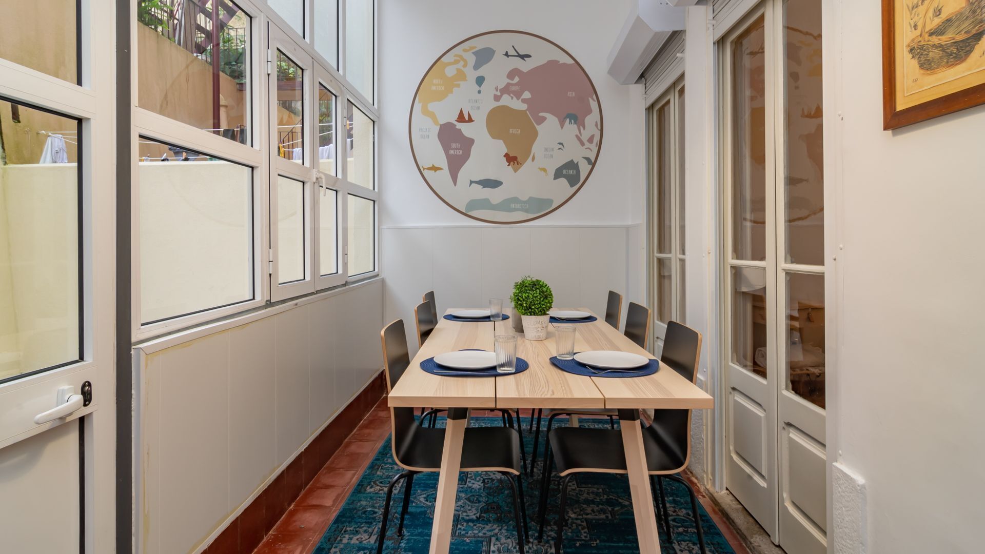 A dining area with a round wall map, a wooden table, chairs, and a small plant.