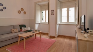 Una sala de estar con sofá, una mesita de centro y un televisor sobre un soporte de madera.