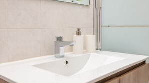 Une salle de bain moderne avec un lavabo blanc, un robinet chromé et deux distributeurs de savon blancs.