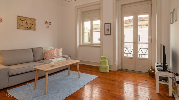 Un salon comprenant un canapé, une table basse, un téléviseur et une fenêtre donnant sur des immeubles.