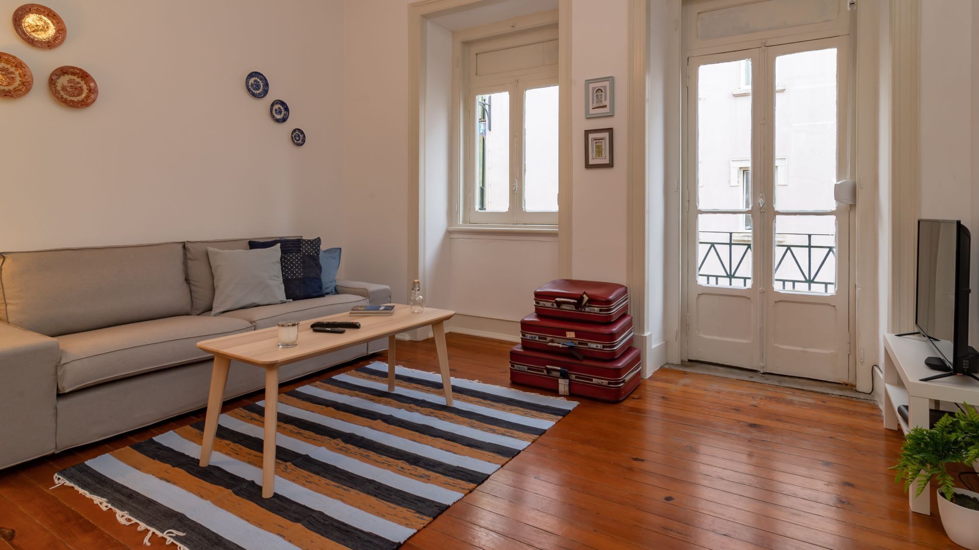 Ein Wohnzimmer mit einer Couch, einem Couchtisch, einem Streifen Teppich, einem Stapel roter Koffer und einem Fernseher auf einem Schrank.