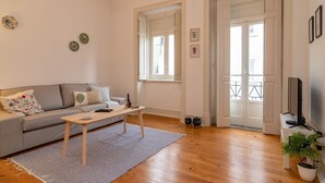 Ein Wohnzimmer mit grauem Sofa, einem Holztisch, einem gemusterten Teppich und einer Topfpflanze.