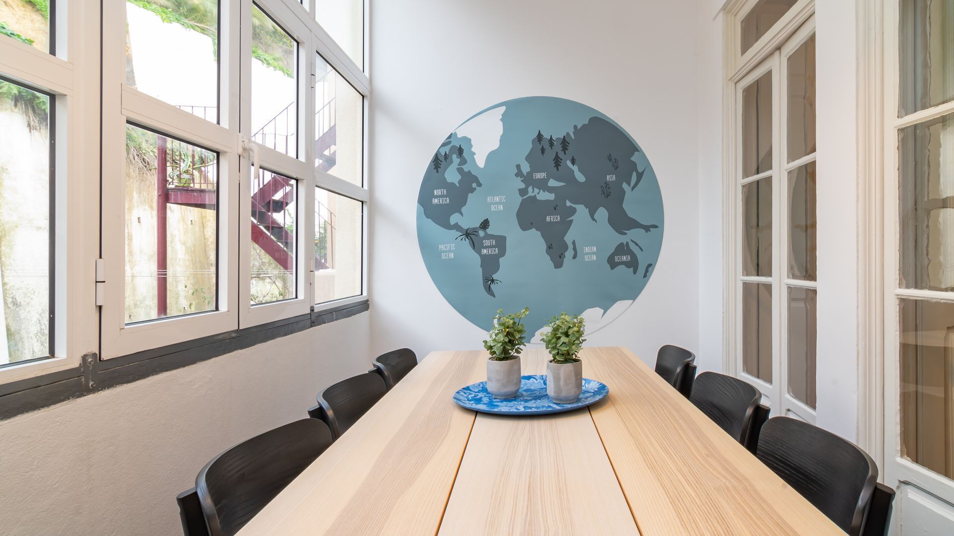 Uma sala de conferências com uma mesa redonda, cadeiras pretas e um mural de mapa mundi na parede.
