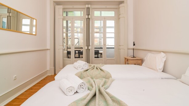 Ein Hotelzimmer mit zwei Betten, einem Spiegel, einem Nachttisch mit Lampe und Blick durch eine Glastür.