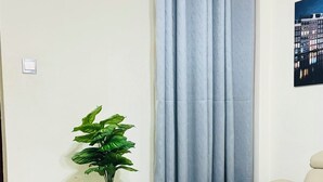 A room with a beige sofa, a white round table with gold legs, a potted plant on a small white table, and a curtain. - New Luxury Apartment very secure at State House Nairobi (kilimani)