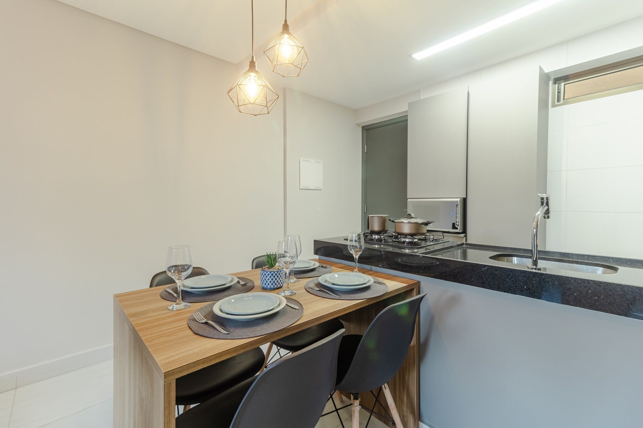 Una cocina moderna con comedor, que presenta una mesa de madera dispuesta para cuatro comensales, una estufa empotrada y un lavamanos de acero inoxidable.