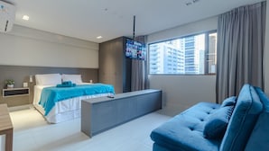 A modern hotel room with a bed, a sofa, a TV mounted on the wall, and a large window with curtains. - Apart no Mardisa Design por Carpediem (João Pessoa)