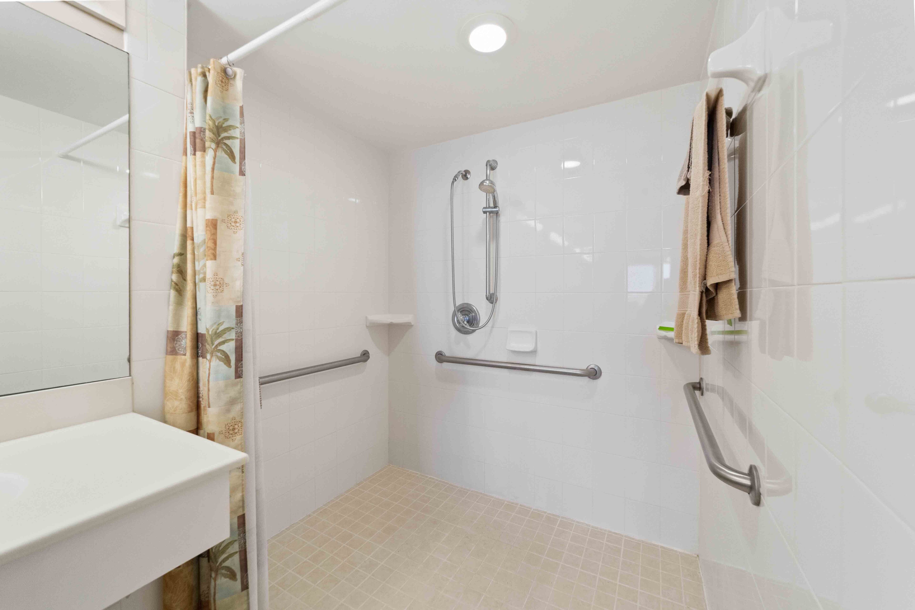Et lille, lukket bruseområde med toilet og håndvask, udstyret med gelænder og brusehoved.