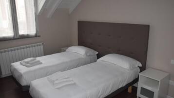 A bedroom with two single beds, a nightstand, and a window with blinds.