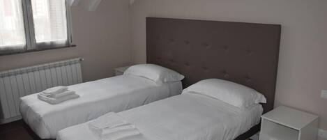 Une chambre avec deux lits simples, une table de chevet et une fenêtre avec des stores.