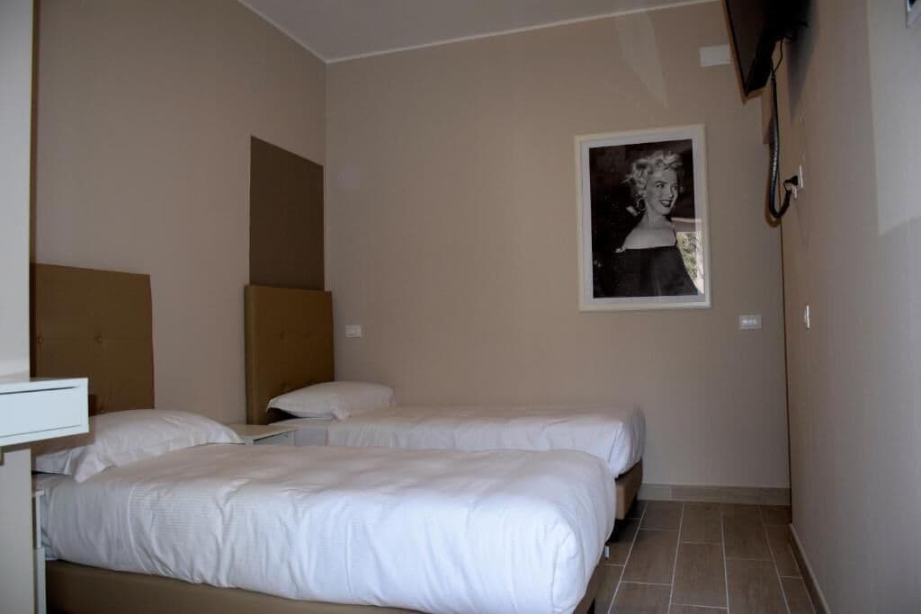 A hotel room with two beds, a headboard, a bedside table, a wall-mounted TV, and a framed picture.