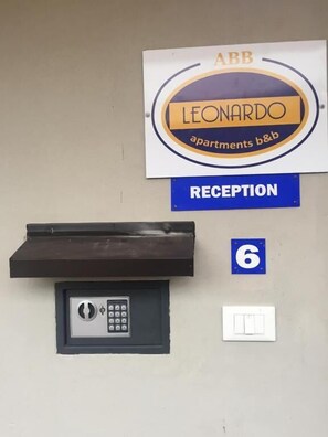 Un área de recepción con un cartel que dice 'Leonardo Apartments b&b', un mostrador de recepción, una cerradura con teclado numérico y un letrero con el número 6.