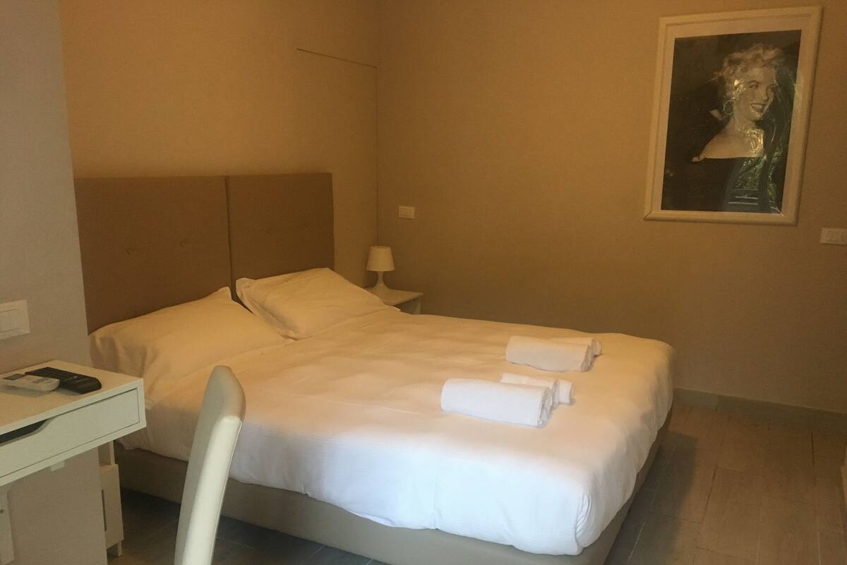 A hotel room with a bed, a desk, a chair, and a painting on the wall.